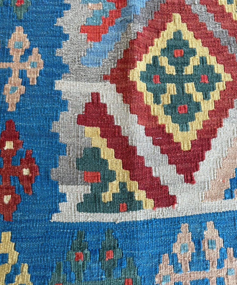 Close-up kilim rug weave with blue, cream, red and yellow geometric diamond motifs