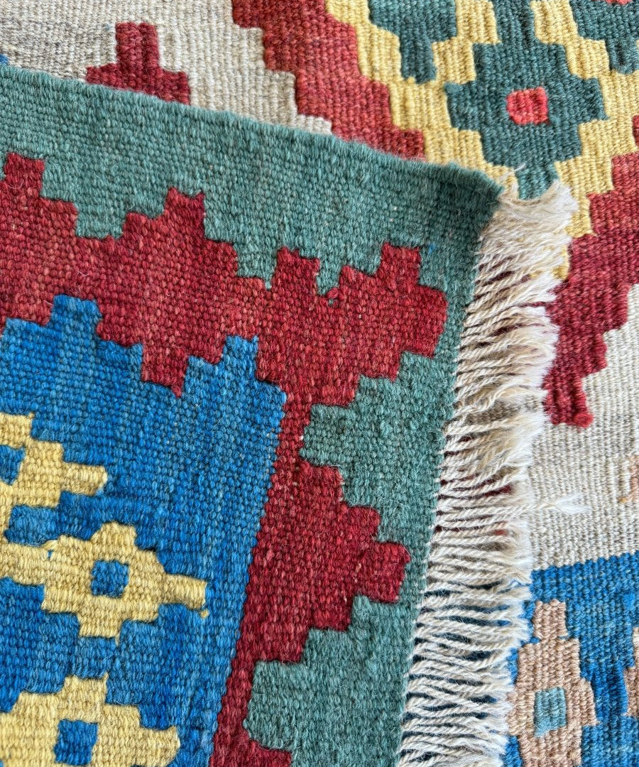 Kilim rug close-up with teal and red geometric blocks, cream border, and white fringe