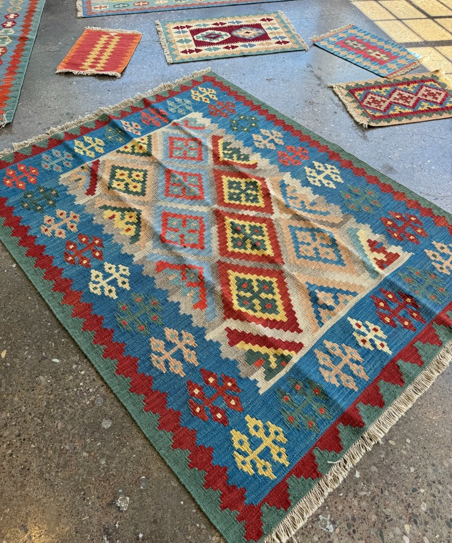 Kilim rug corner on display, blue background with red and cream geometric motifs, fringed