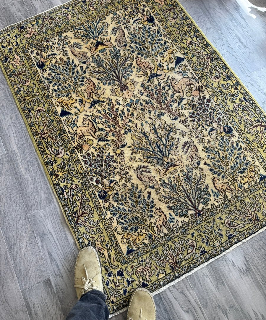 Persian Qom area rug laid flat, cream field with blue, gold, and animal motifs
