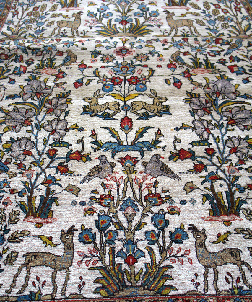 Full rug view with ivory field, branching floral designs, and small animals in rows.