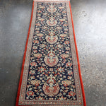 Persian Qom runner rug viewed from above, navy floral pattern with red outer border