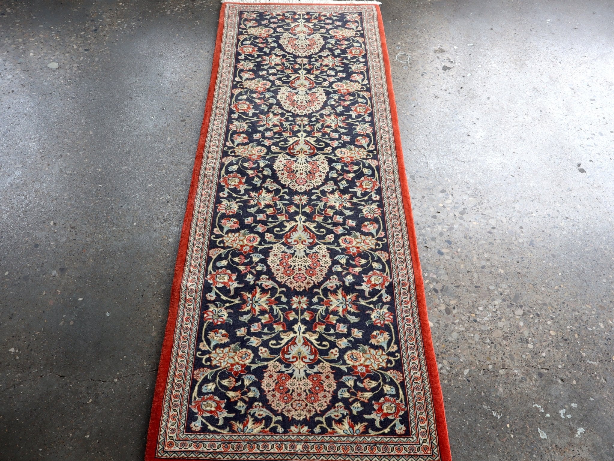 Persian Qom runner rug viewed from above, navy floral pattern with red outer border