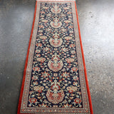 Persian Qom runner rug viewed from above, navy floral pattern with red outer border