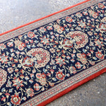 Persian Qom runner rug corner detail: navy floral scrollwork, red border trim