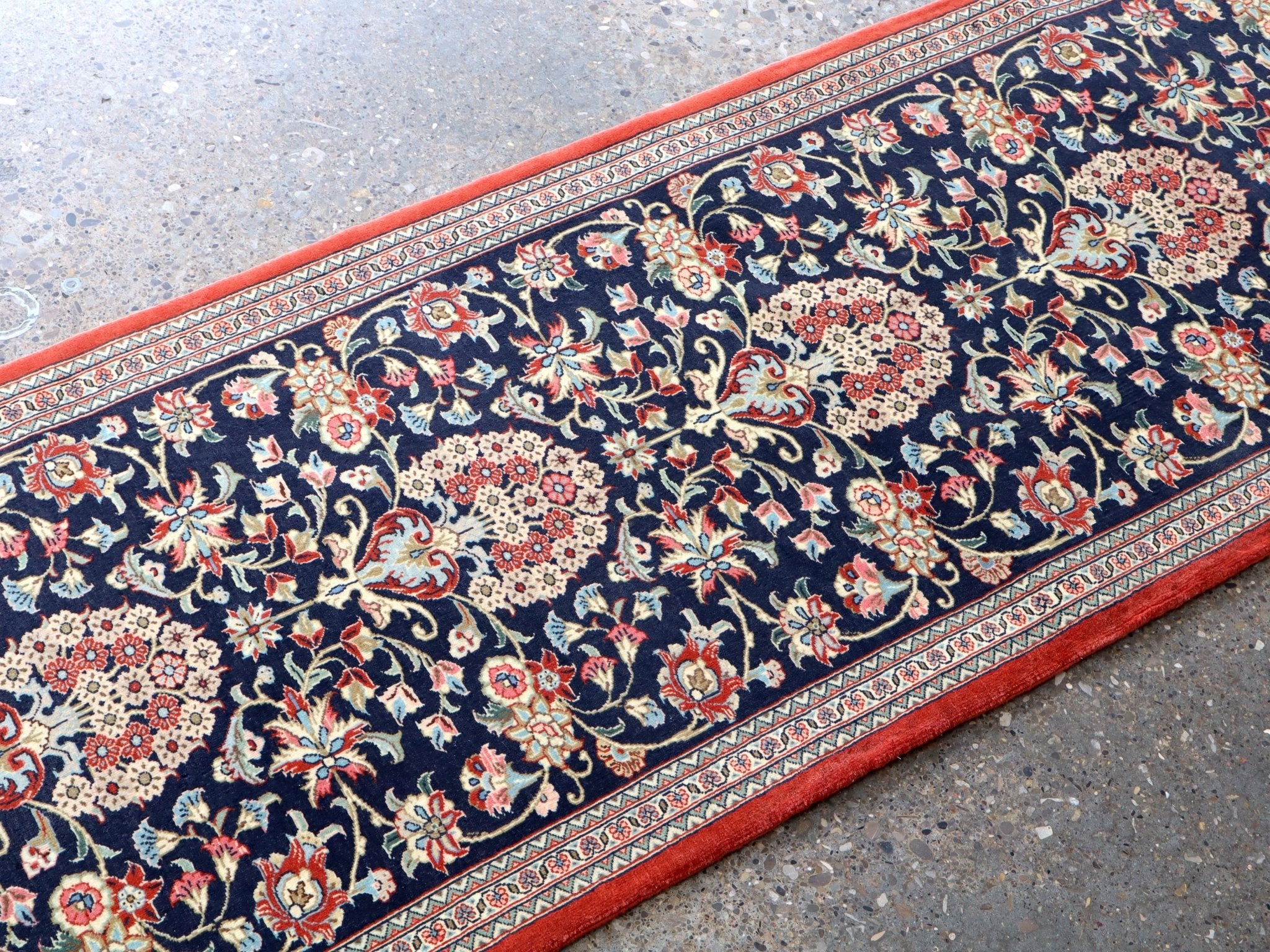 Persian Qom runner rug corner detail: navy floral scrollwork, red border trim