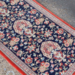 Persian Qom runner rug corner view: navy floral vines, multicolor rosettes, red border