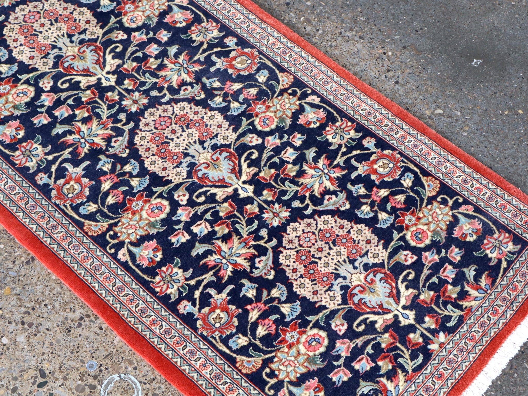 Persian Qom runner rug corner view: navy floral vines, multicolor rosettes, red border