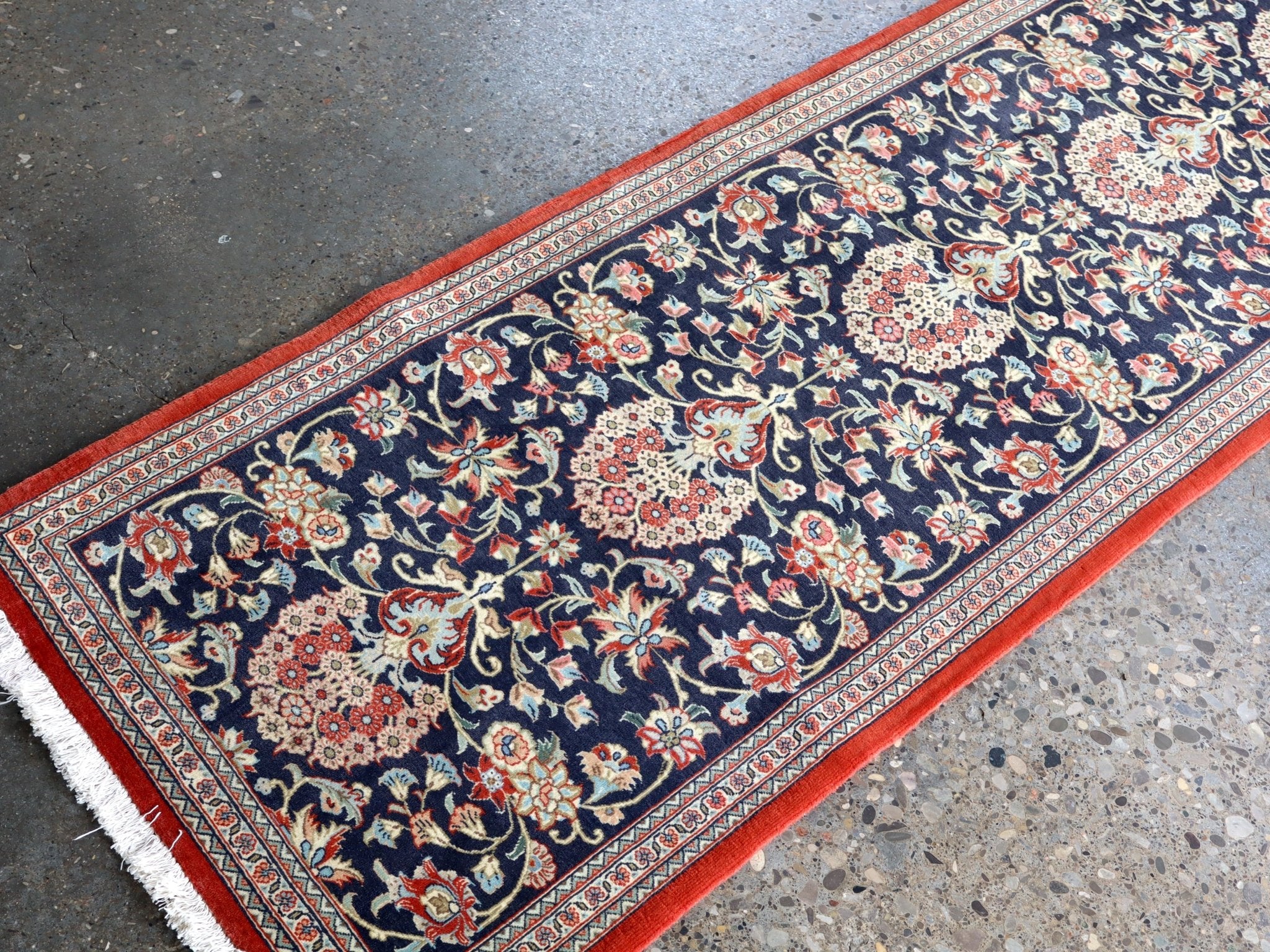Persian Qom runner rug edge close-up: navy floral medallions, red border and cream stripe