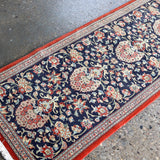 Persian Qom runner rug edge close-up: navy floral medallions, red border and cream stripe