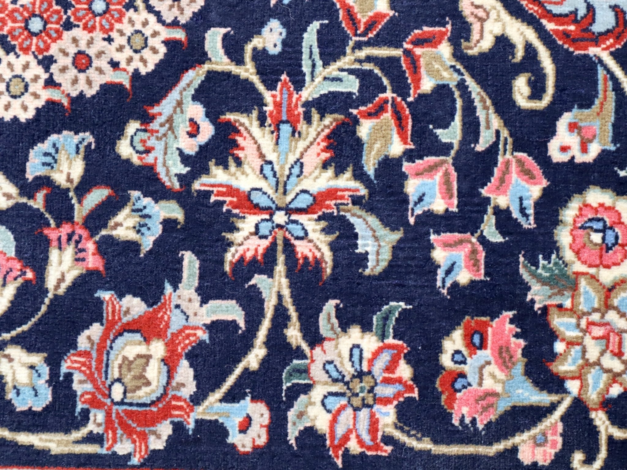 Persian Qom runner rug close-up: navy background with red, cream, and blue blossoms