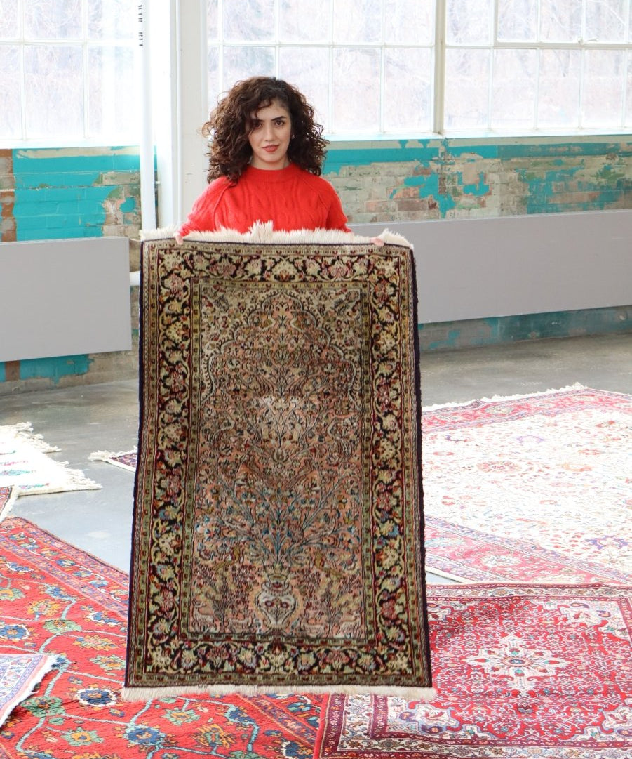Persian Qum silk rug held upright, showing ornate medallion and red-edge border