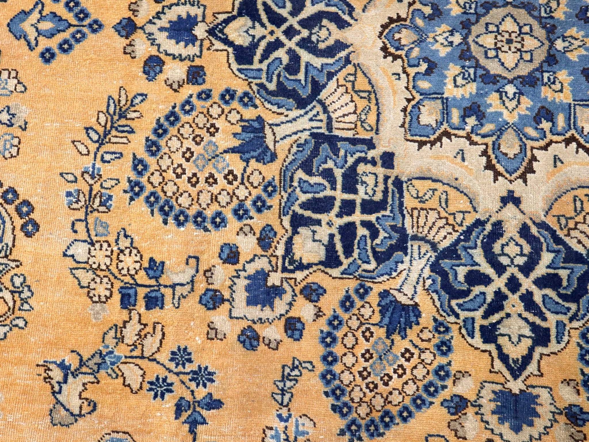 Persian-style rug close-up of blue vine and floral motifs on tan woven surface
