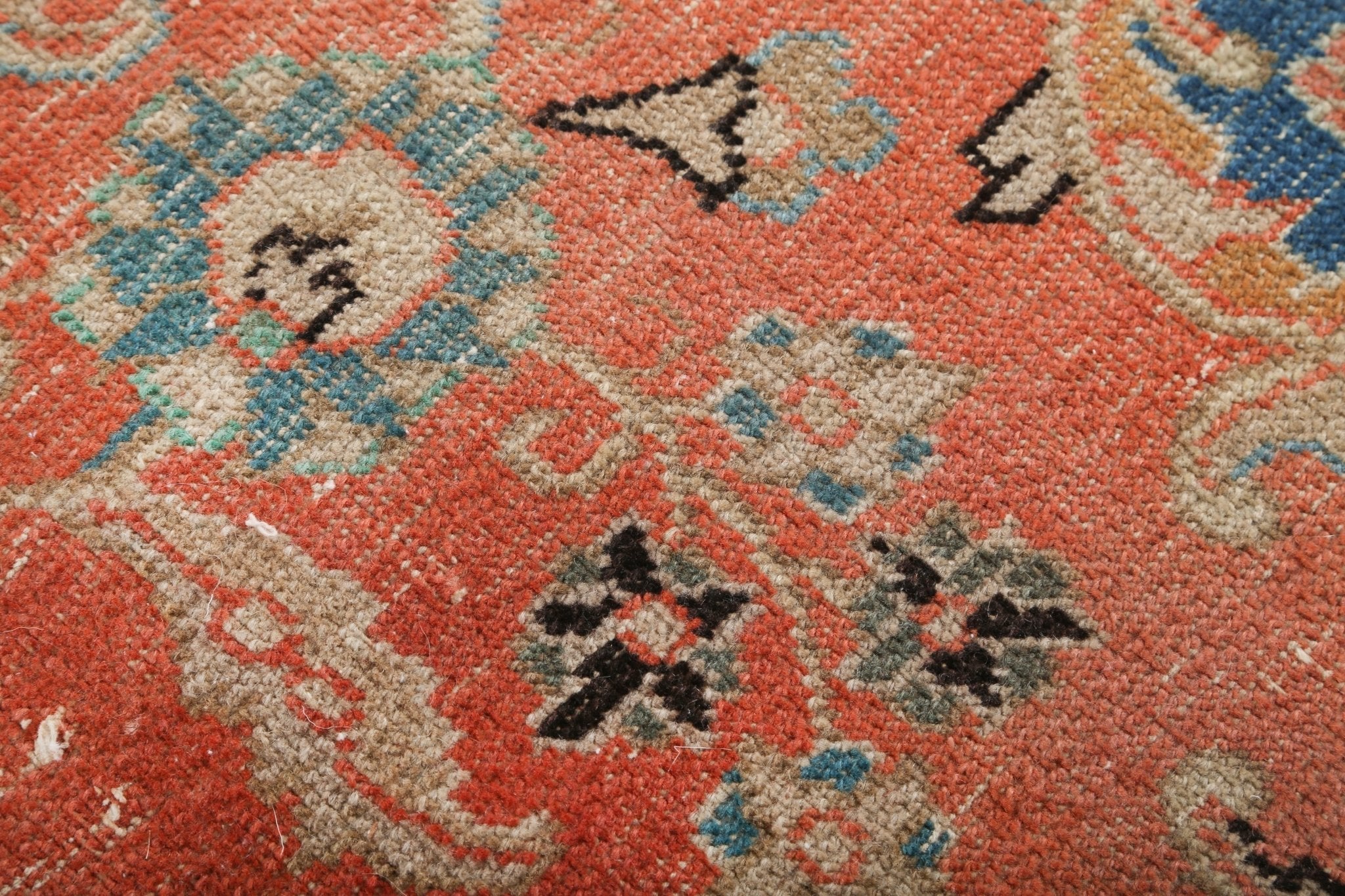 Close-up of coral rug with cream and teal motifs, dark floral accents
