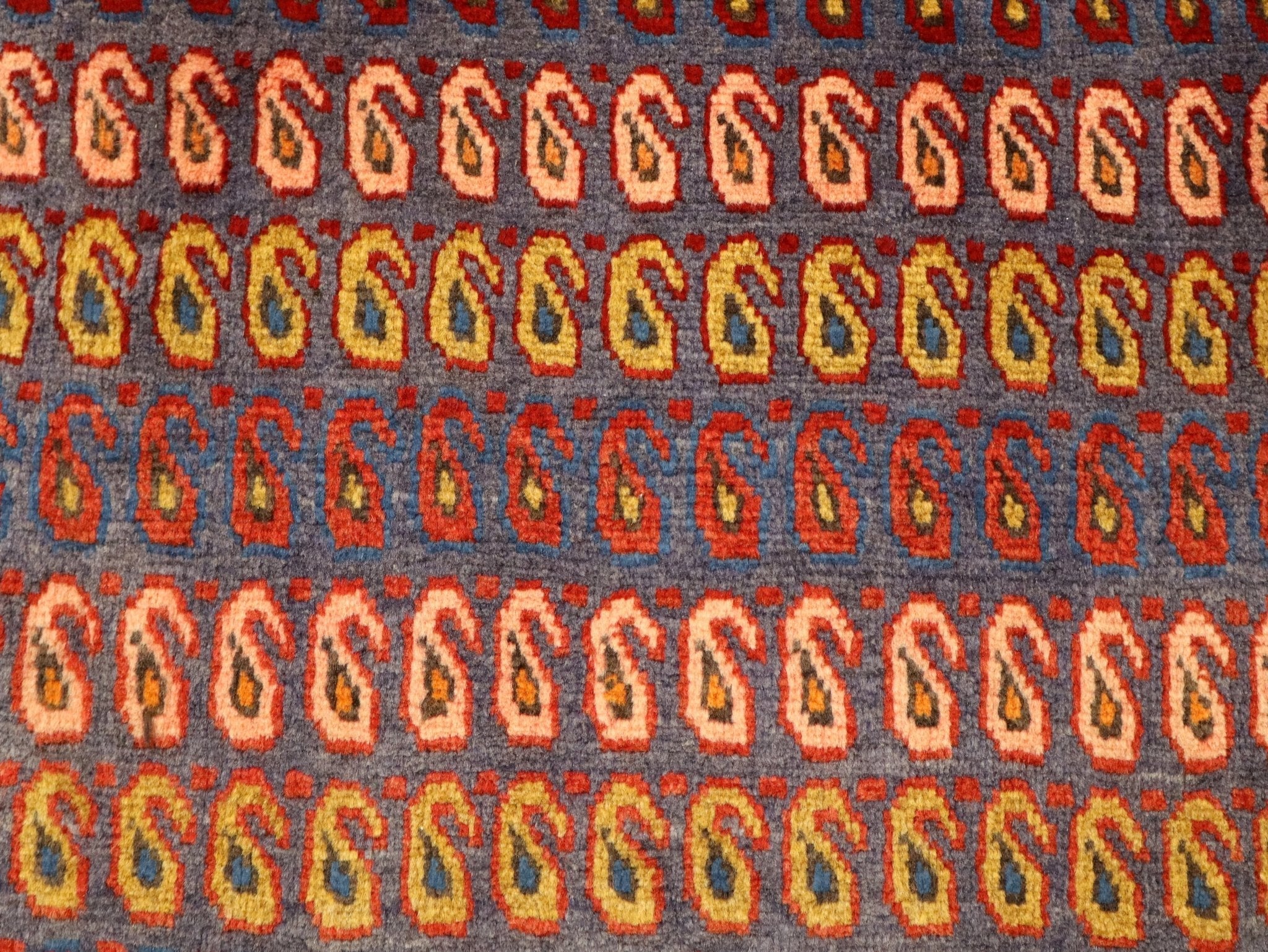 Close-up of Persian rug pattern: repeating hooked shapes in red, orange, and blue on gray.