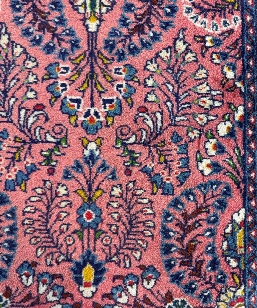 Persian Sarouk rug close-up showing dense floral vines on red ground with navy trim