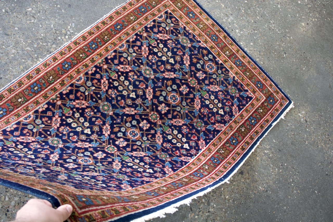 Sarouk rug corner with navy ground, multicolor medallion pattern, and red-green edge border.