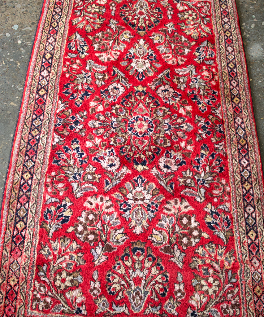 Tall Persian Sarouk rug with red background, white floral medallions, and border.