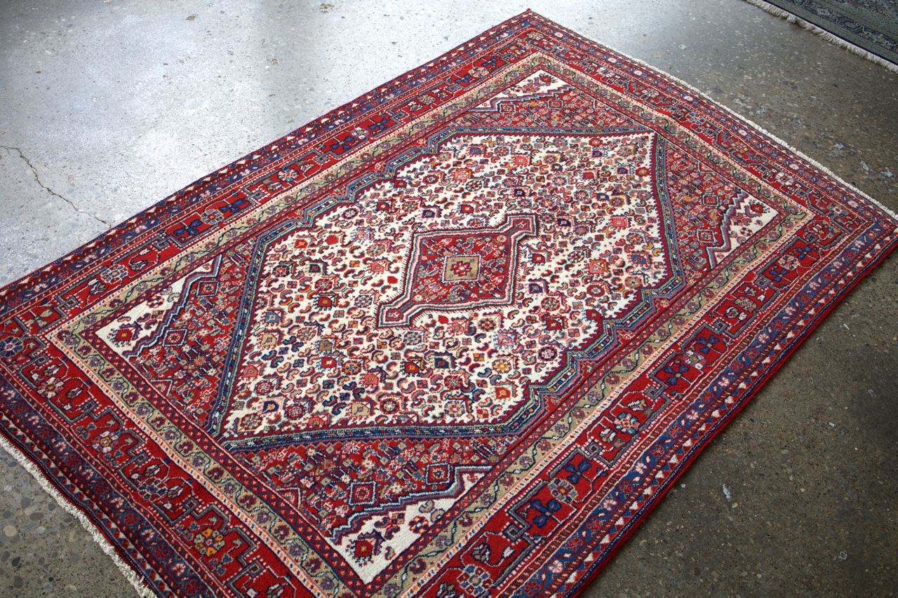 Persian-style Sarouk rug with red border, cream center medallion, and blue accents