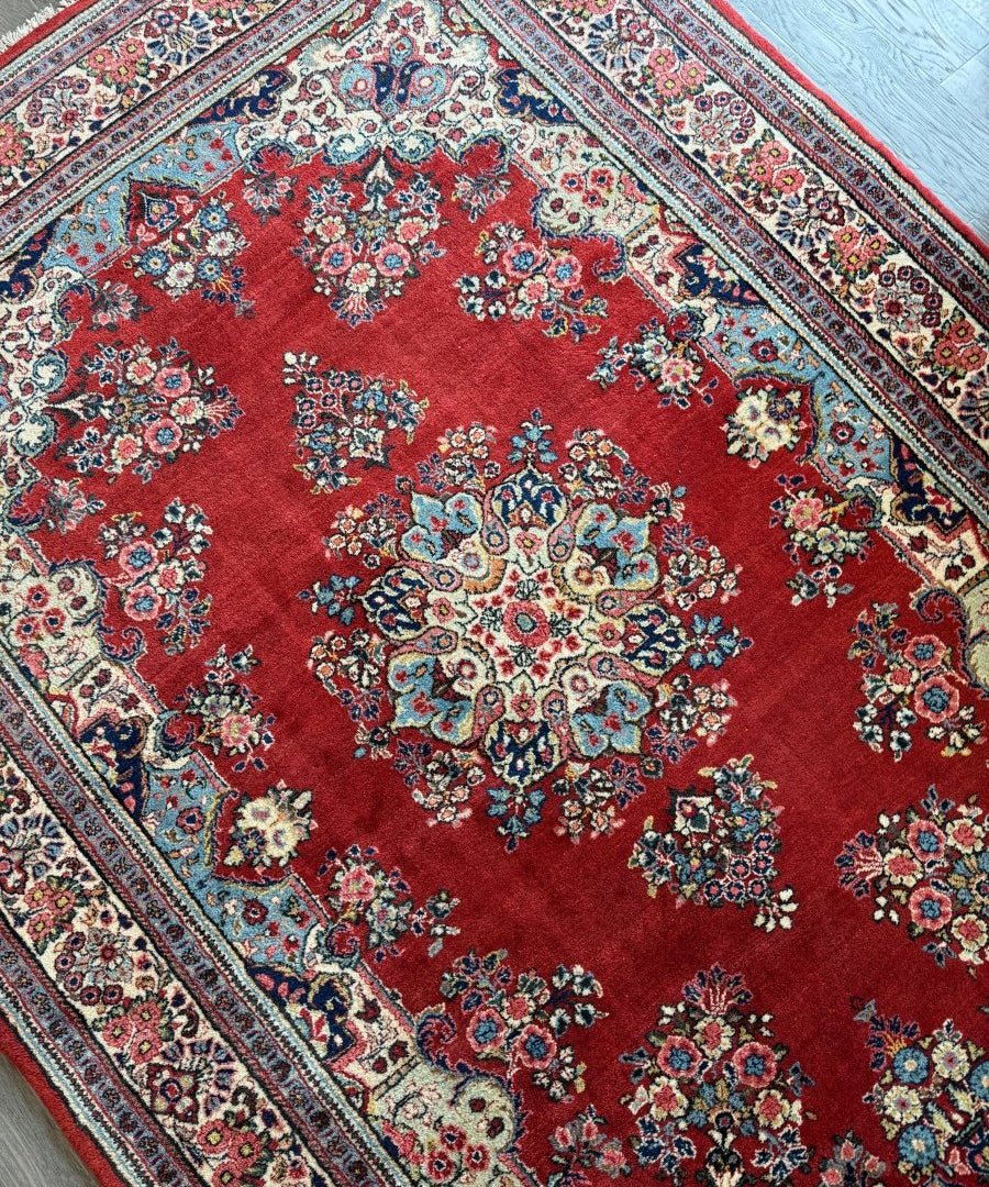 Red Sarouk rug with dense floral medallion pattern and navy, teal, cream accents.