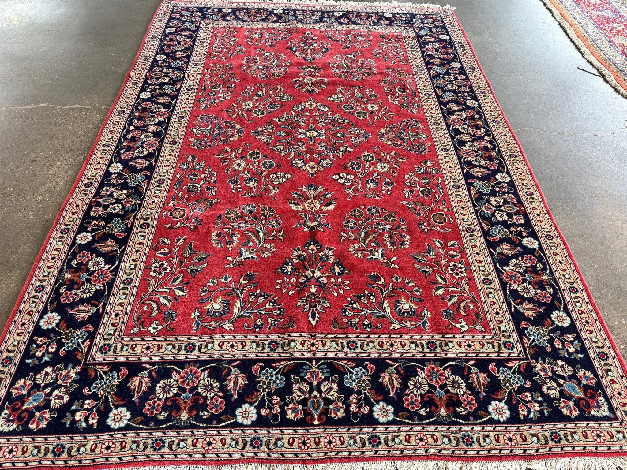 Red Sarouk rug with navy field, cream corner panels, floral border and fringe