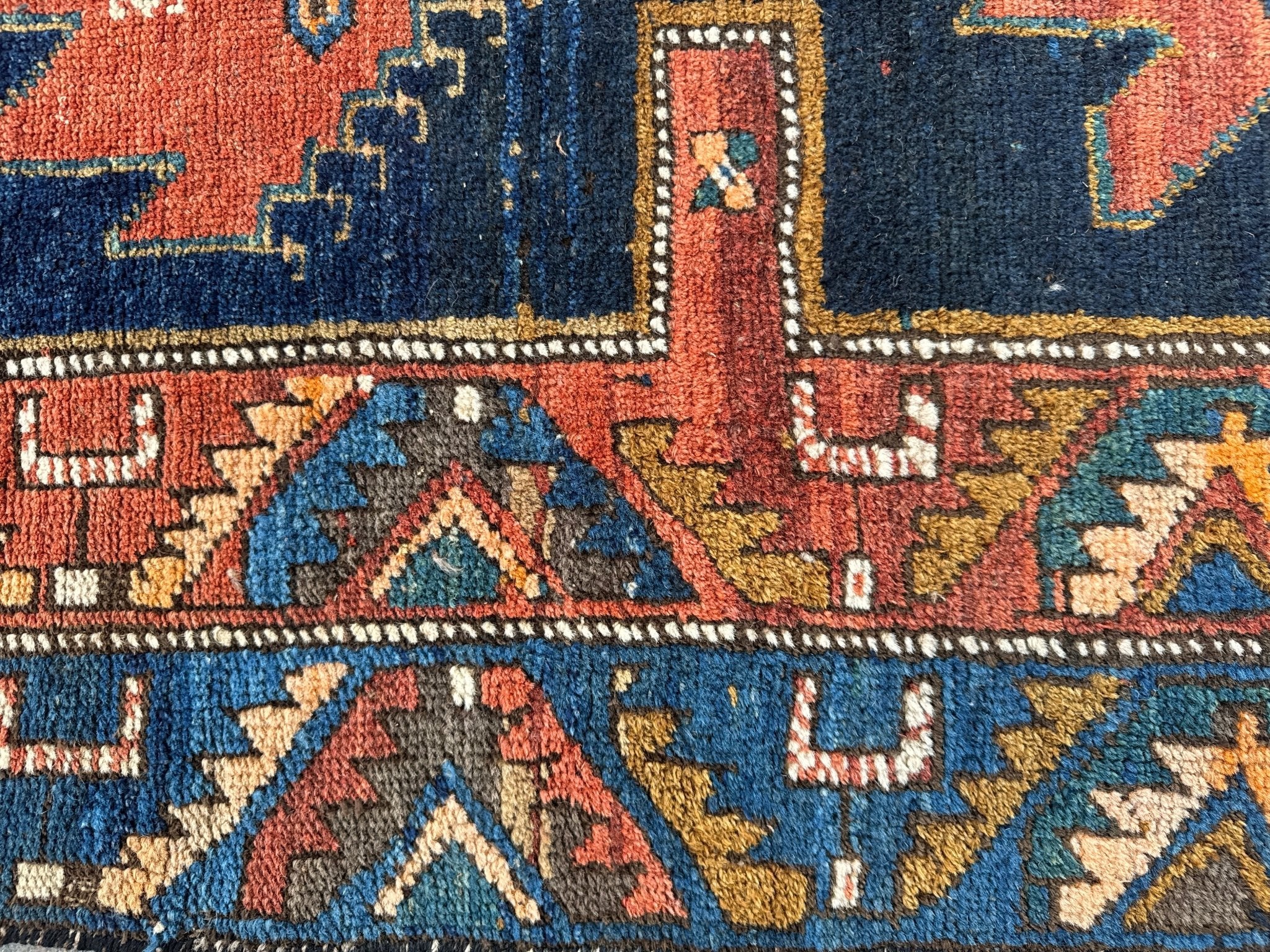 Close-up of Persian runner rug border with red, navy, teal, and cream repeating shapes