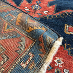Corner detail of Persian runner rug with navy, rust, teal, and cream patterning and fringe