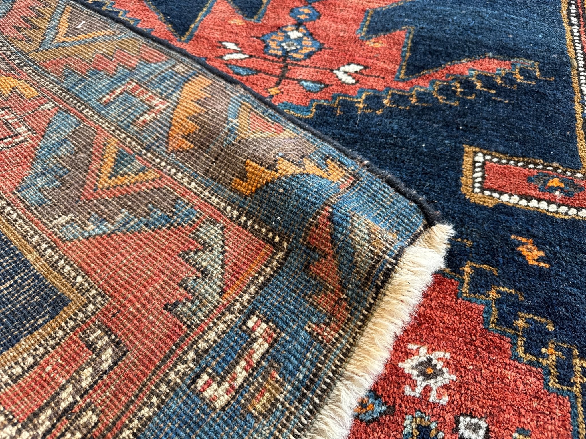 Corner detail of Persian runner rug with navy, rust, teal, and cream patterning and fringe