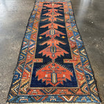 Persian runner rug laid flat on floor with navy field, rust medallions, and blue borders