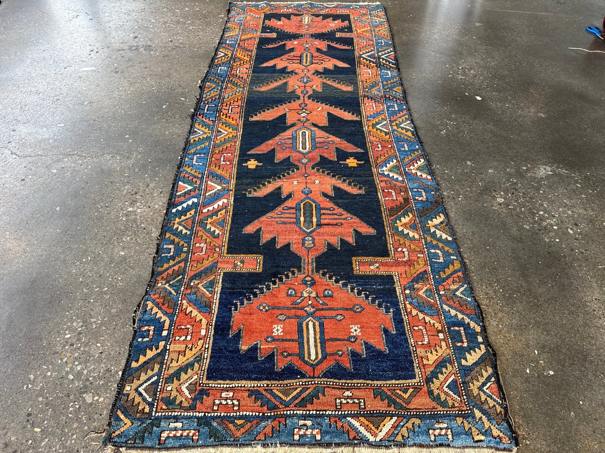 Persian runner rug laid flat on floor with navy field, rust medallions, and blue borders