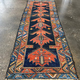 Persian runner rug laid flat on floor with navy field, rust medallions, and blue borders