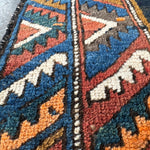 Close-up of Persian runner rug weave with navy, rust, teal, and cream geometric motifs