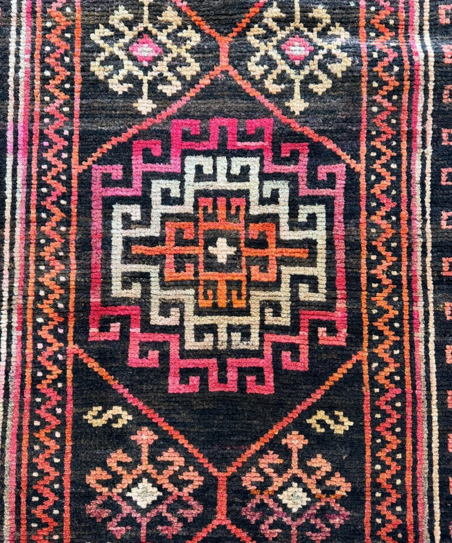 Close view of runner rug medallion with dark navy, pink, red, and cream geometric design.