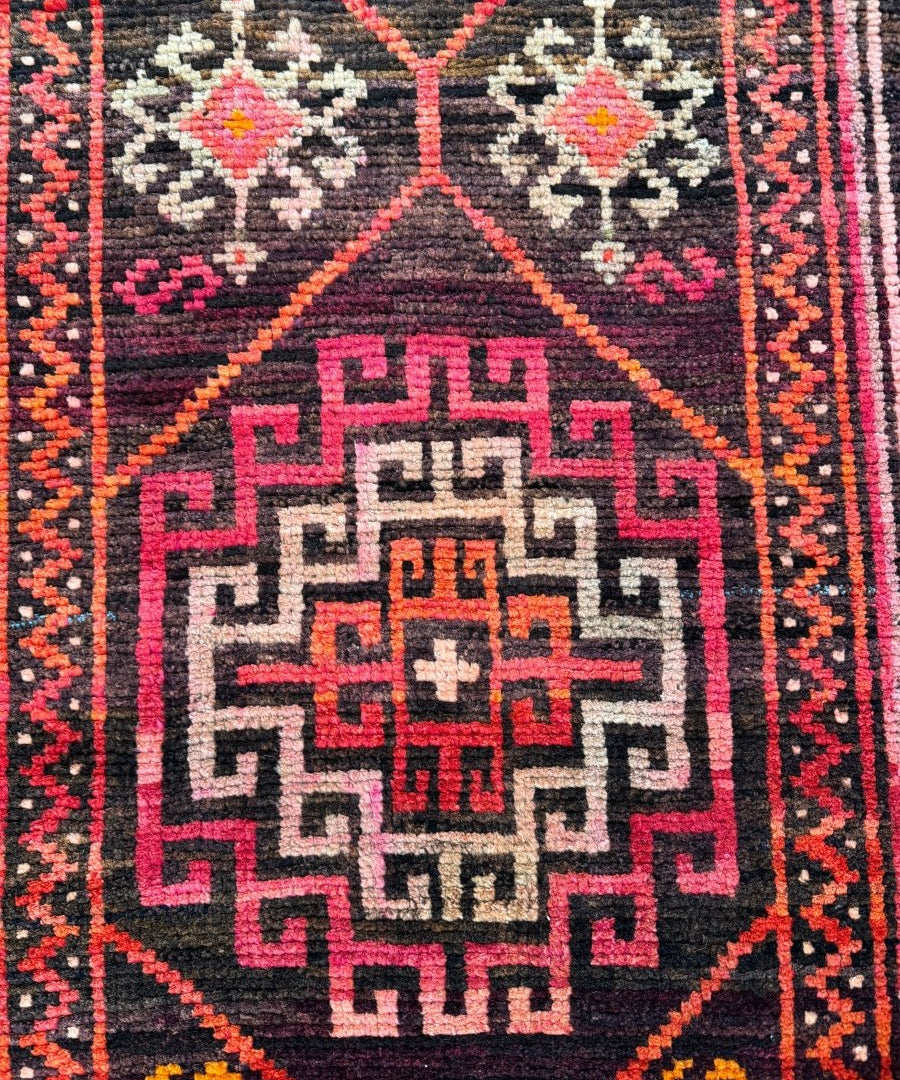 Close view of runner rug center medallion with dark navy, magenta, and cream motifs.