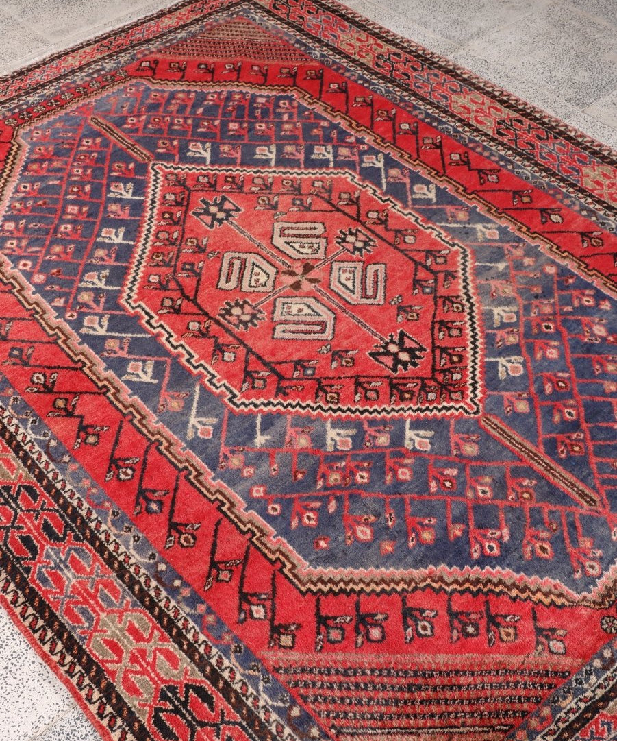 Persian Shahreh-Babak rug angled view with red field, blue borders and diamond motifs