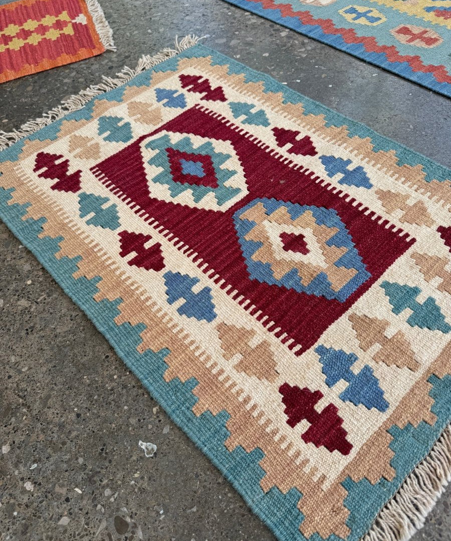 Small Persian-style kilim rug with geometric medallions, maroon, blue, beige, and fringe edges.