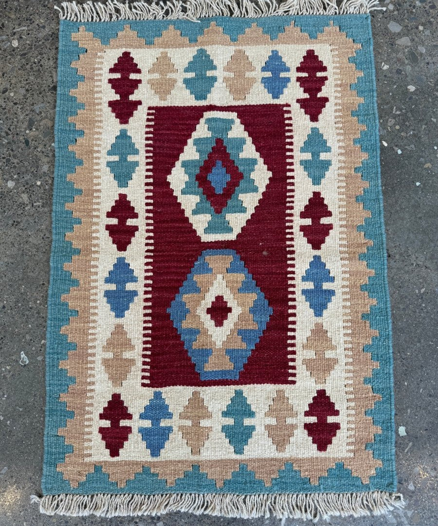 Square kilim rug featuring central diamond medallions in maroon, blue, beige with fringe.