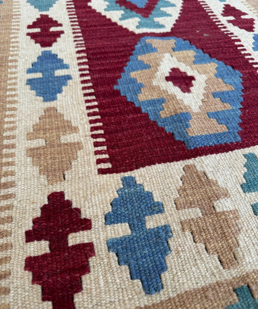 Close-up of geometric kilim pattern with maroon, blue, tan shapes and woven texture.