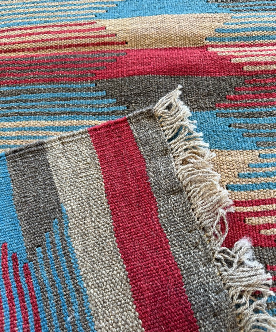 Persian Shiraz kilim rug corner with frayed fringe and red, blue, beige bands.