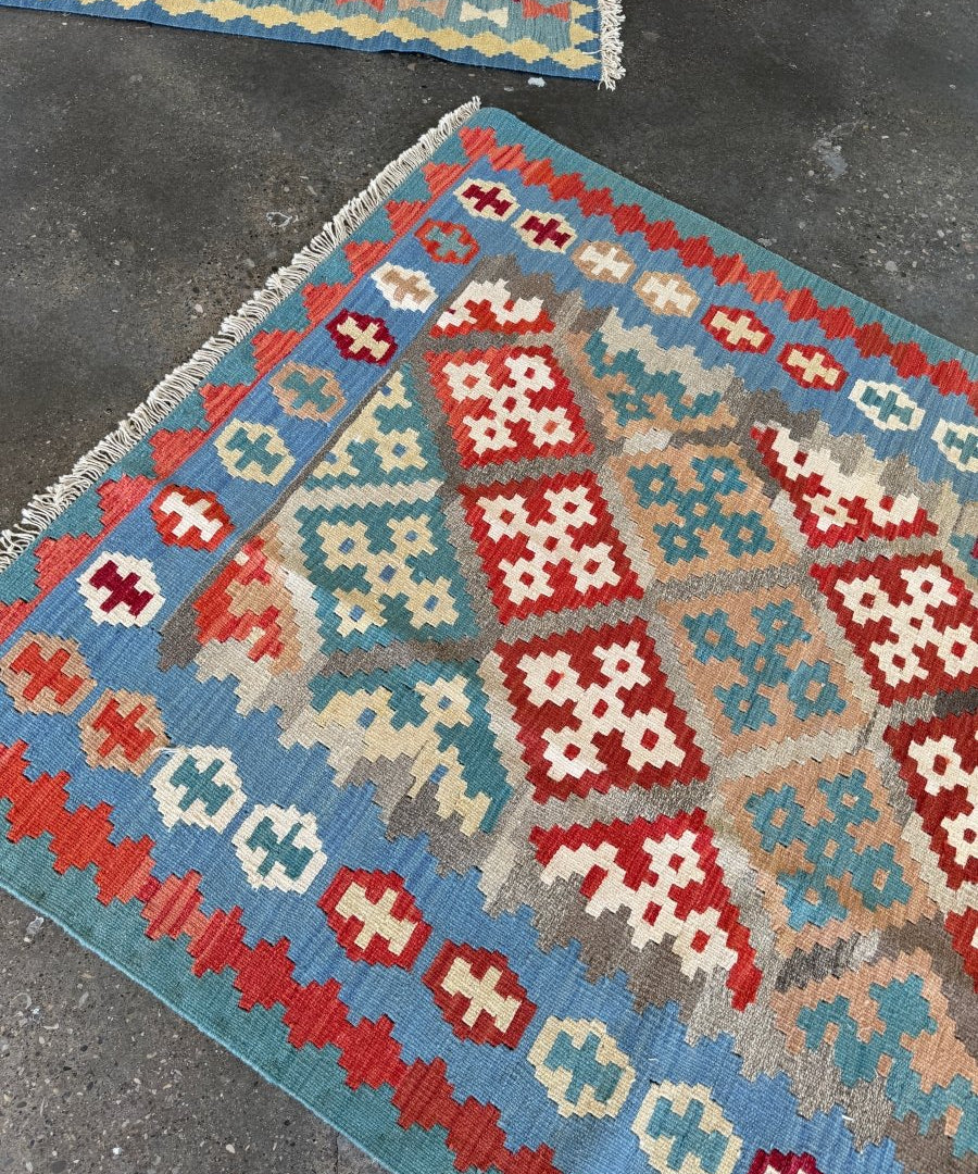 Kilim rug with red, blue, and cream geometric diamond patterns, fringed border