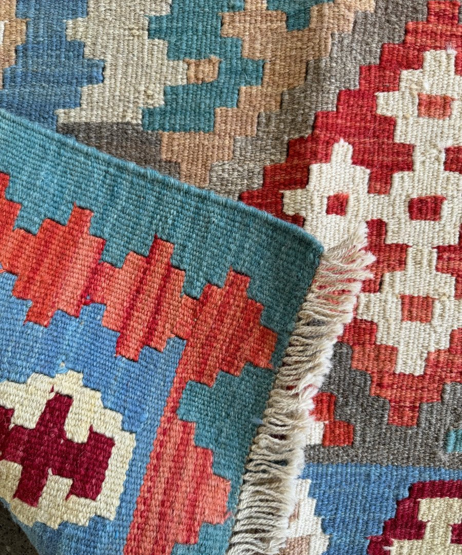 Kilim rug corner detail with fringes and multicolor geometric blocks on blue ground