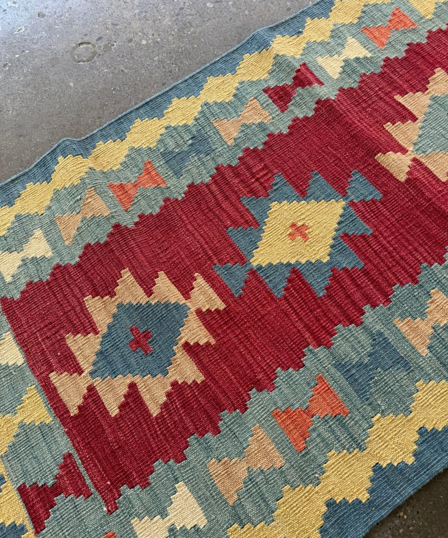 Kilim runner rug corner with geometric stripes in red, blue, yellow, and cream