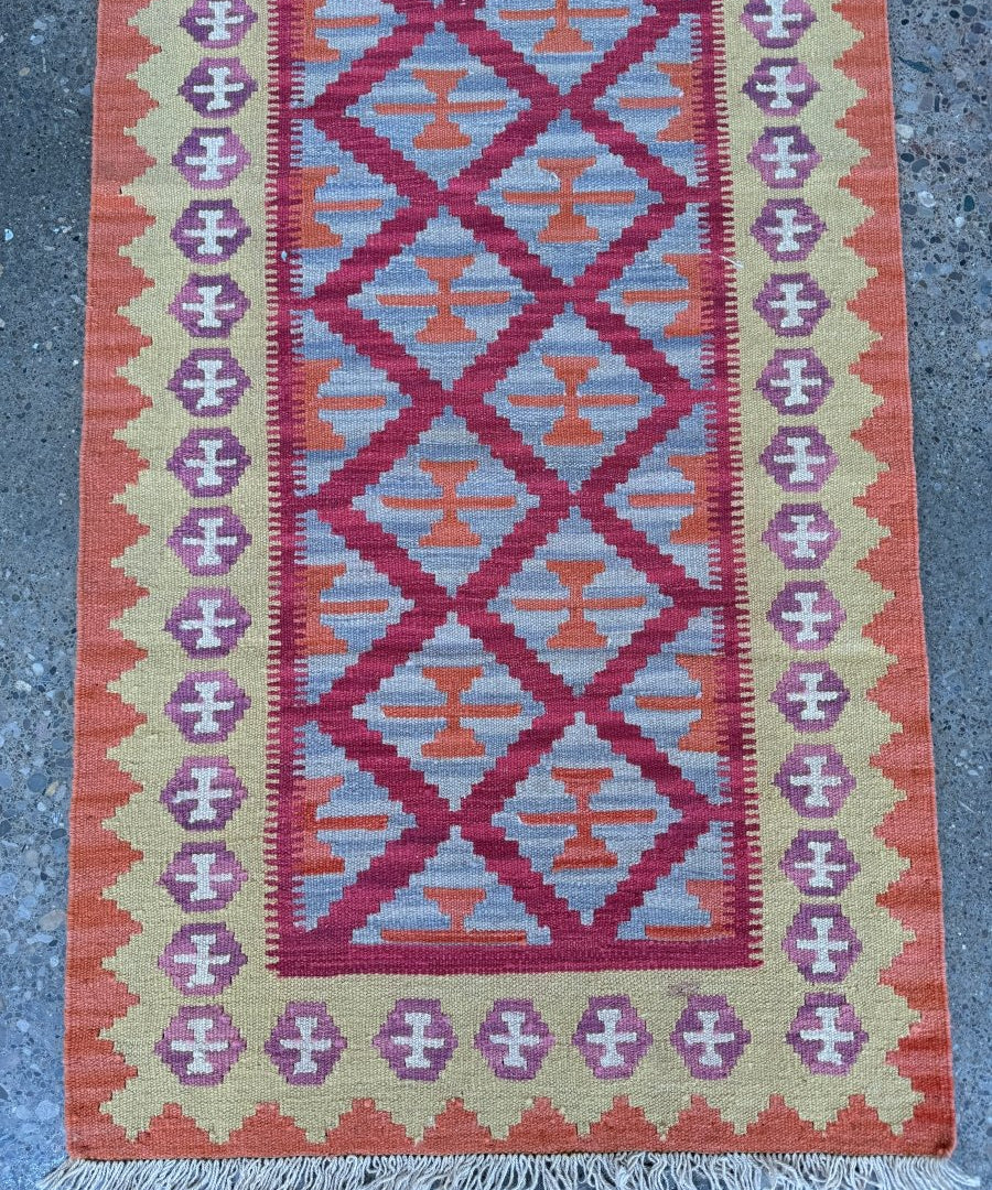 Red and blue geometric runner rug with repeating diamond medallions and purple border; fringe.