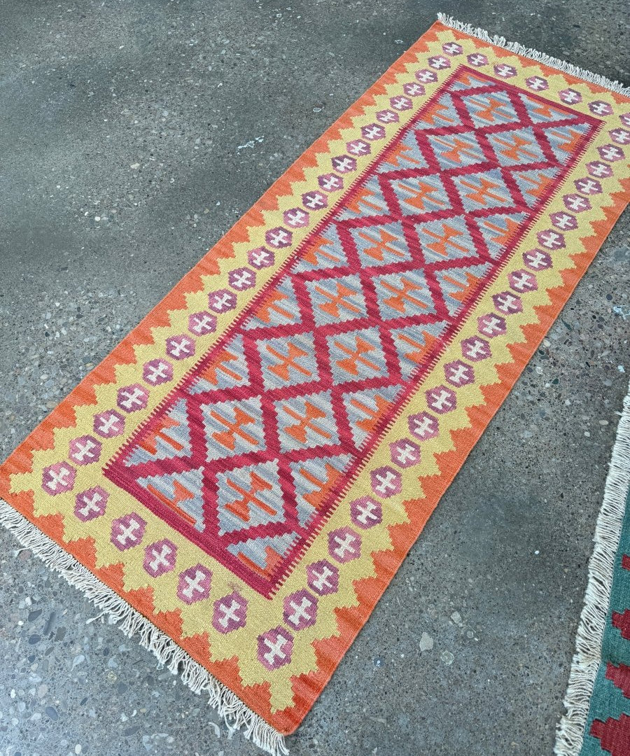 Orange runner rug with diagonal kilim chevrons in blue, pink, and purple; short fringe.