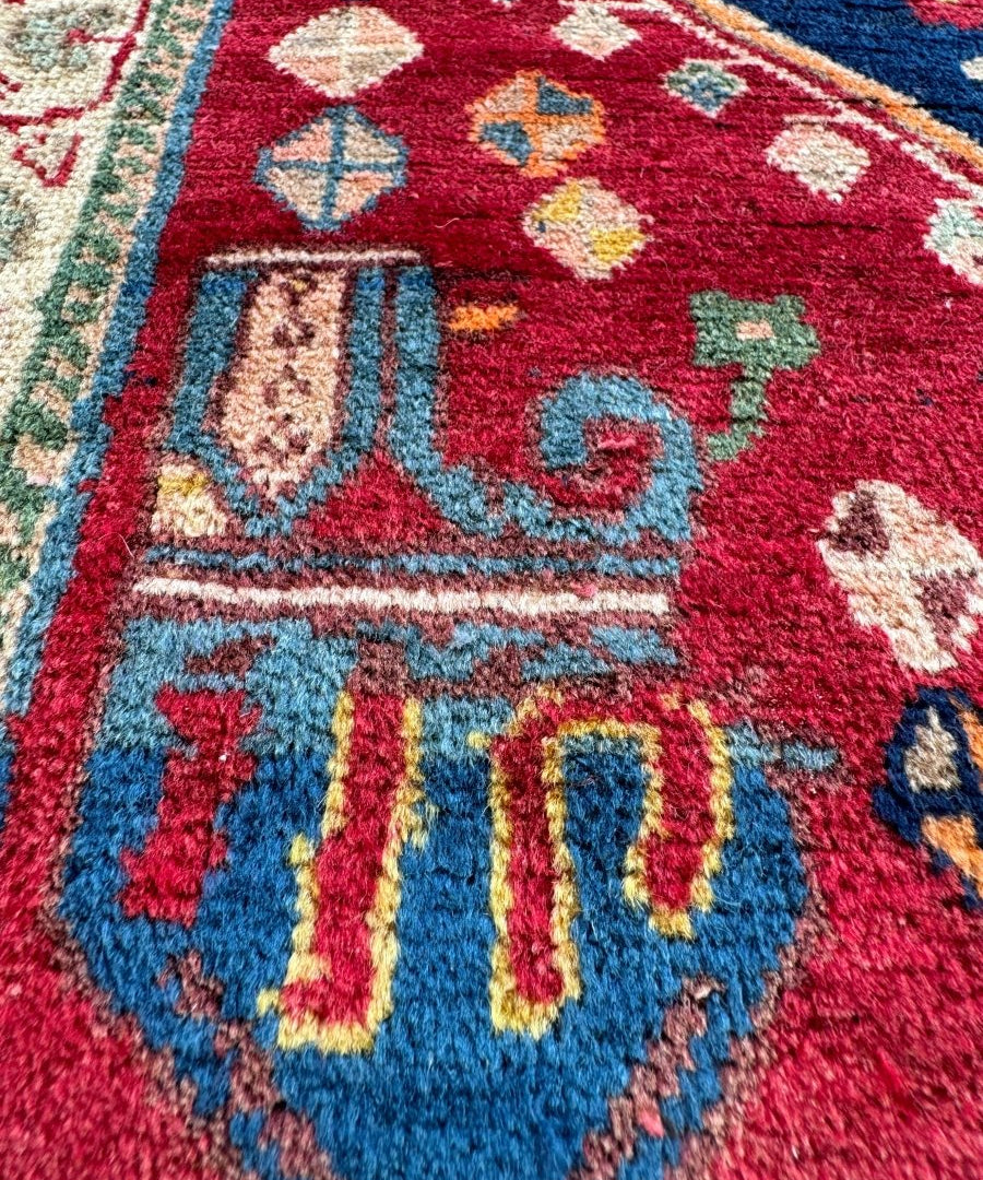 Close-up Persian Shiraz rug corner with red field, blue shapes, and light geometric accents.