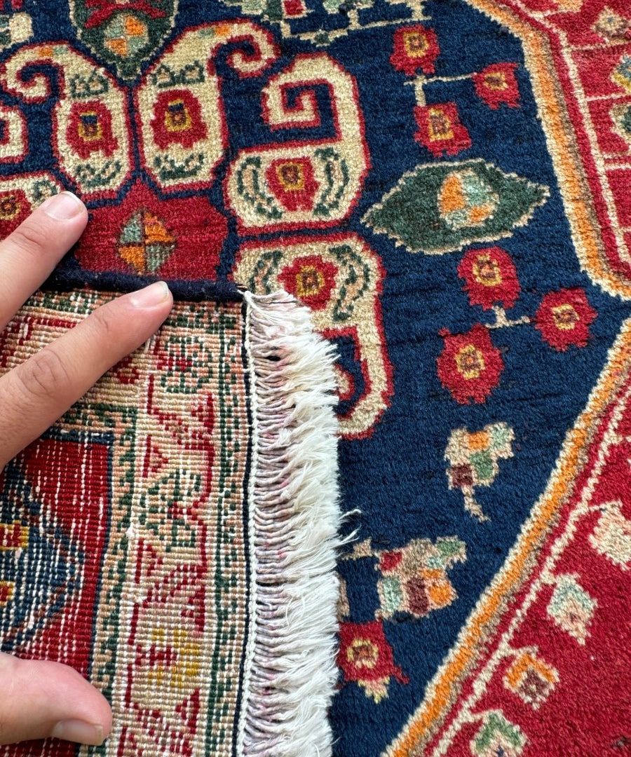 Persian Shiraz rug edge detail showing dark blue field, red border, and short fringe.