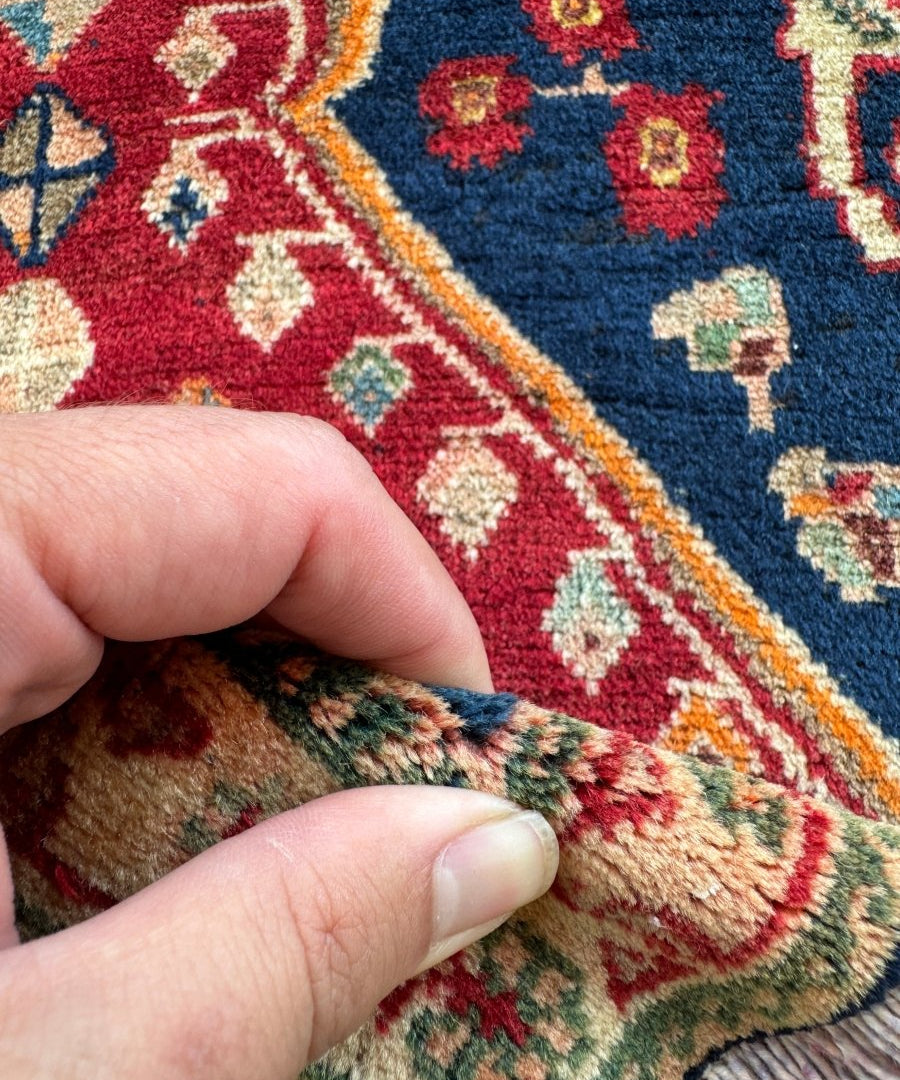 Persian Shiraz rug corner detail with red-and-blue pattern border and trimmed fringe edge.