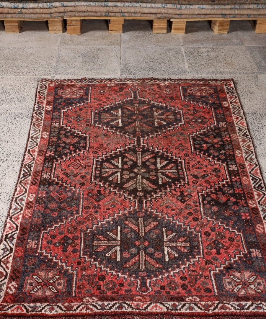 Persian Shiraz rug laid flat, red field with dark medallions and white patterned border