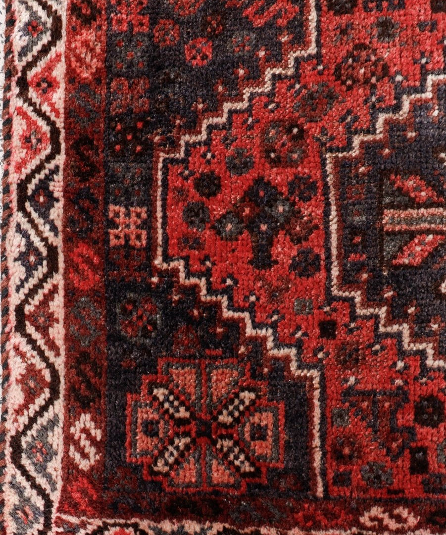 Persian Shiraz rug close-up of red and black geometric motifs with cream edge trim