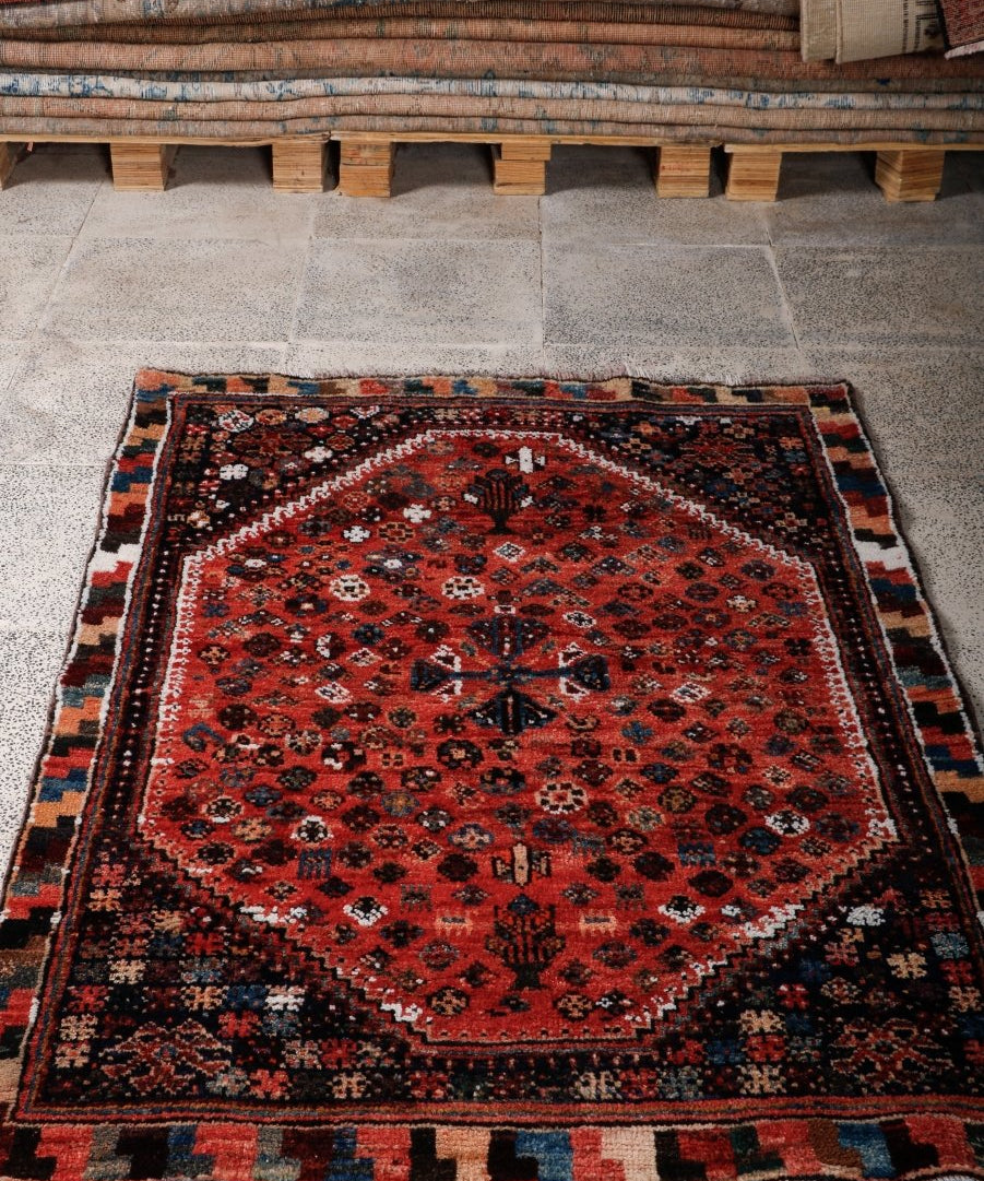 Persian-style rug with red center medallion, navy corner accents, and short fringe on edges
